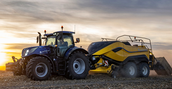 blå traktor med gult släp på åker i solnedgång.