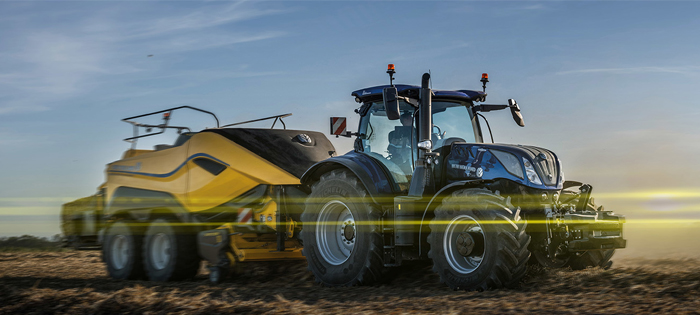 Blå New Holland traktor med gult släp på fält